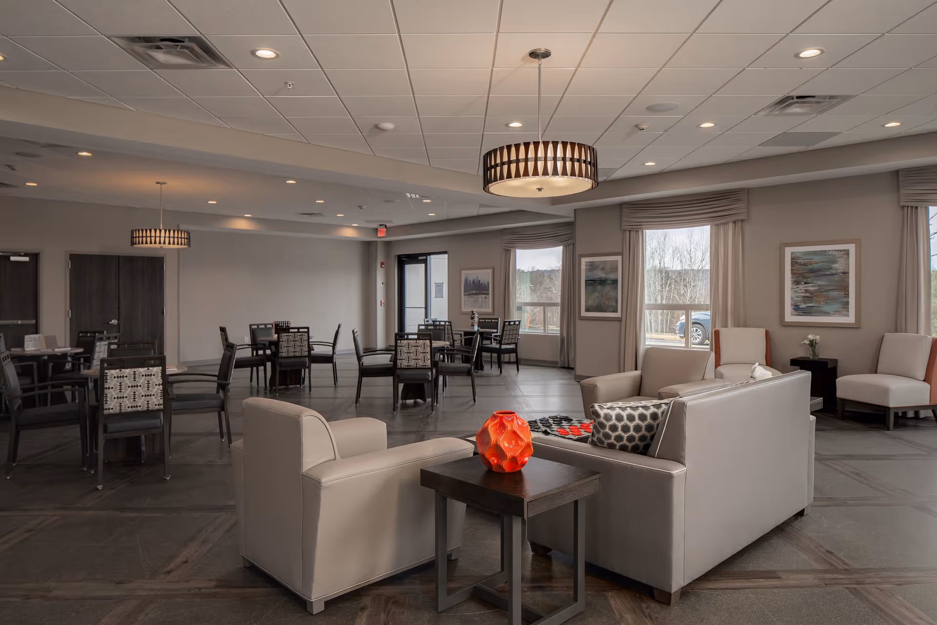 Spacious communal dining and lounge area with tables, chairs and sofas in a senior living facility.