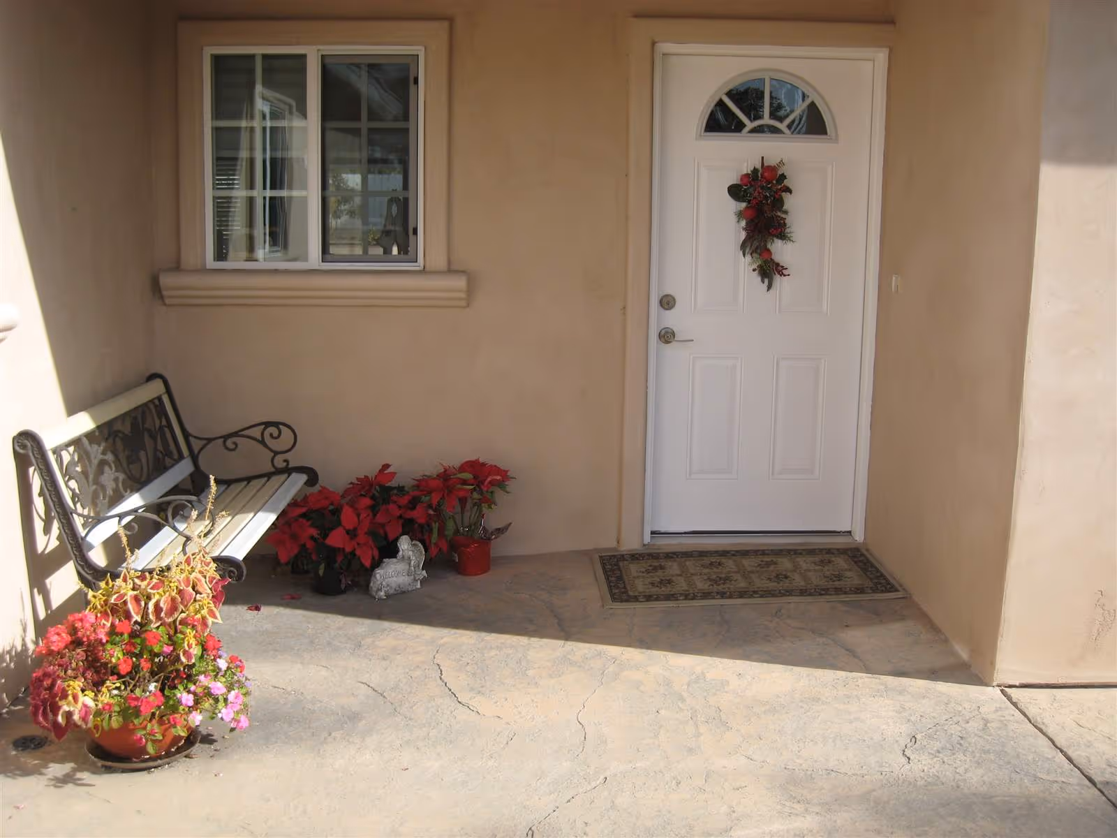 A front entryway with a white door decorated with a wreath, a bench, potted flowers, and a window.