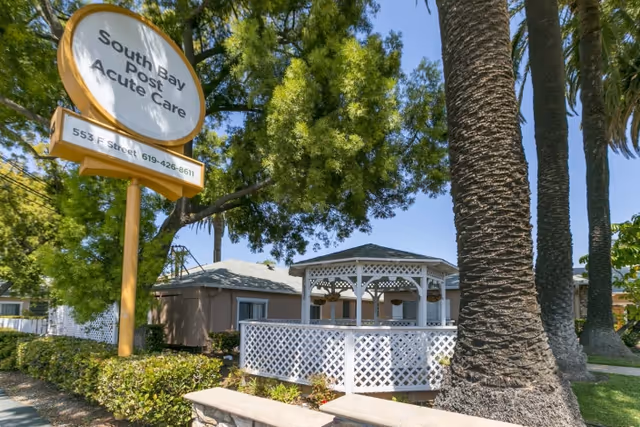 Front exterior of South Bay Post Acute Care showing a large sign, white gazebo, palm trees, and landscaping.