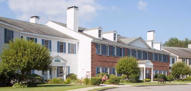 Exterior view of Langdon Place of Keene, showing a long white-brick building with blue shutters.