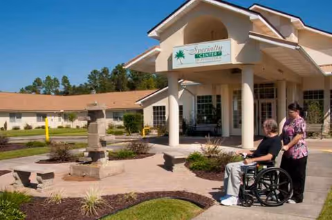 Exterior view of a senior living center entrance with a wheelchair user and caregiver.