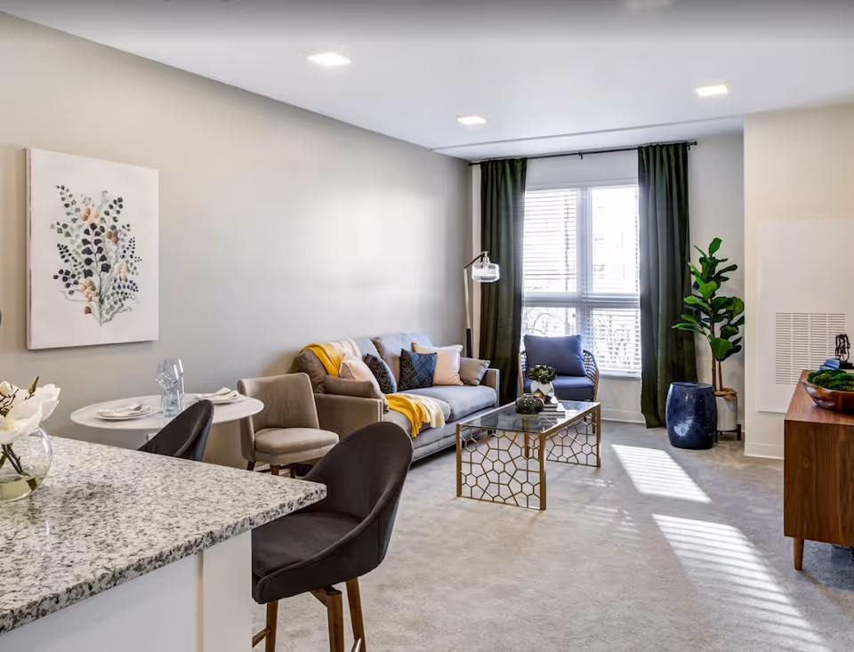 Bright modern living room with a sofa, armchairs, coffee table, and a kitchen counter in the foreground.