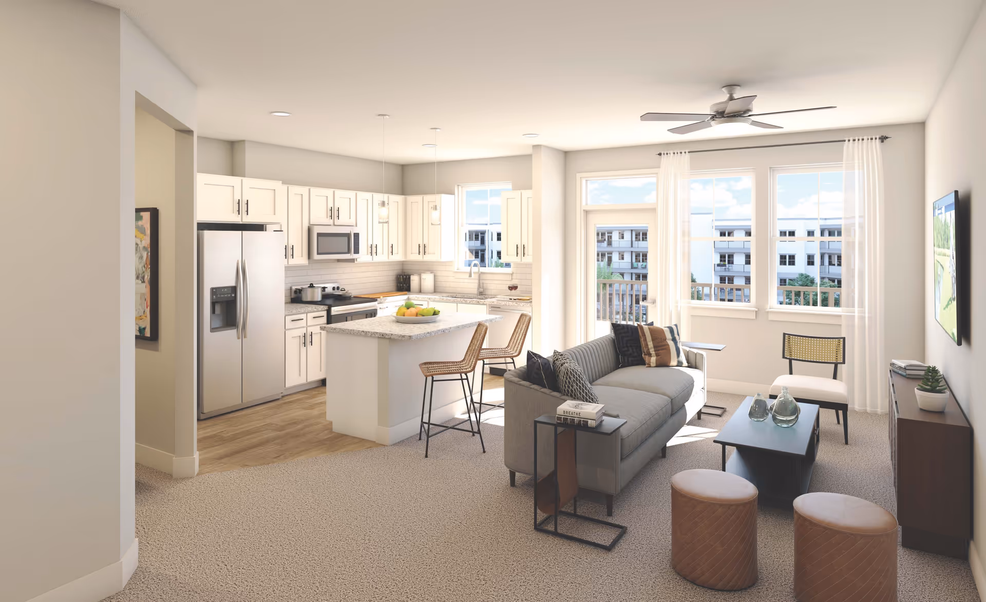 Bright and modern open-concept living space featuring a kitchen with white cabinets, stainless steel appliances, and a granite island with two bar stools. Adjacent living room area includes a gray sofa with pillows, a coffee table with decorative glass bottles, two round ottomans, a chair, and a TV mounted on the wall. Large windows and a glass door with sheer white curtains allow natural light to fill the room, with a ceiling fan overhead.