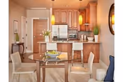 Open-plan kitchen and dining area with wooden cabinets, stainless steel appliances, a central island with pendant lights, and a glass dining table with four chairs.