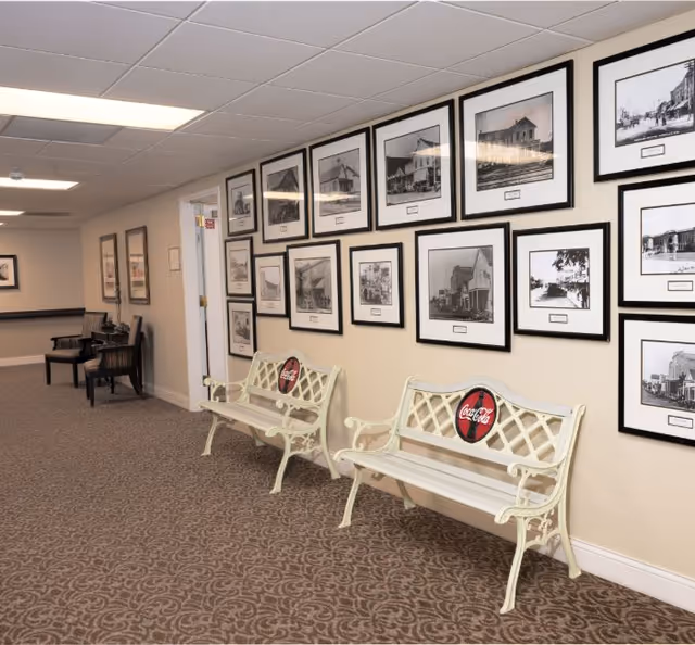 Interior hallway with framed black-and-white photos on the wall and two decorative benches with Coca-Cola medallions.