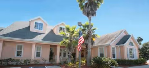 Single-story pink building exterior with palm trees and an American flag.