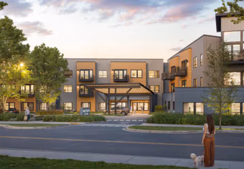 Exterior view of a modern senior living facility named Cogir of Tigard at dusk, showing a three-story building with balconies, a covered entrance, landscaped greenery, and a woman walking a small dog on the sidewalk in front.