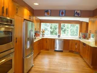 Bright wooden kitchen with stainless steel appliances and a large window overlooking greenery.