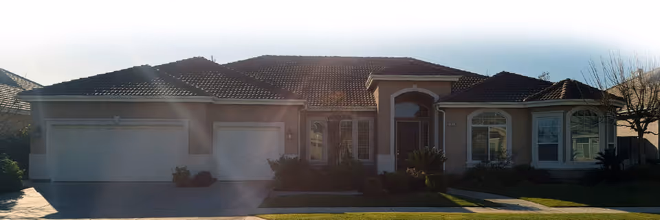 Front exterior of a single-story stucco house with a three-car garage, tiled roof, driveway, and lawn.