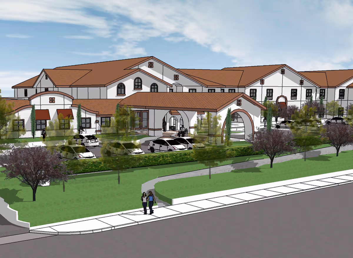 Architectural rendering of The Villas at Stanford Ranch showing a large building with a red-tiled roof, arched entryways, multiple windows, and a parking area with cars. There are trees and green landscaping in front, along with a sidewalk where two people are walking.
