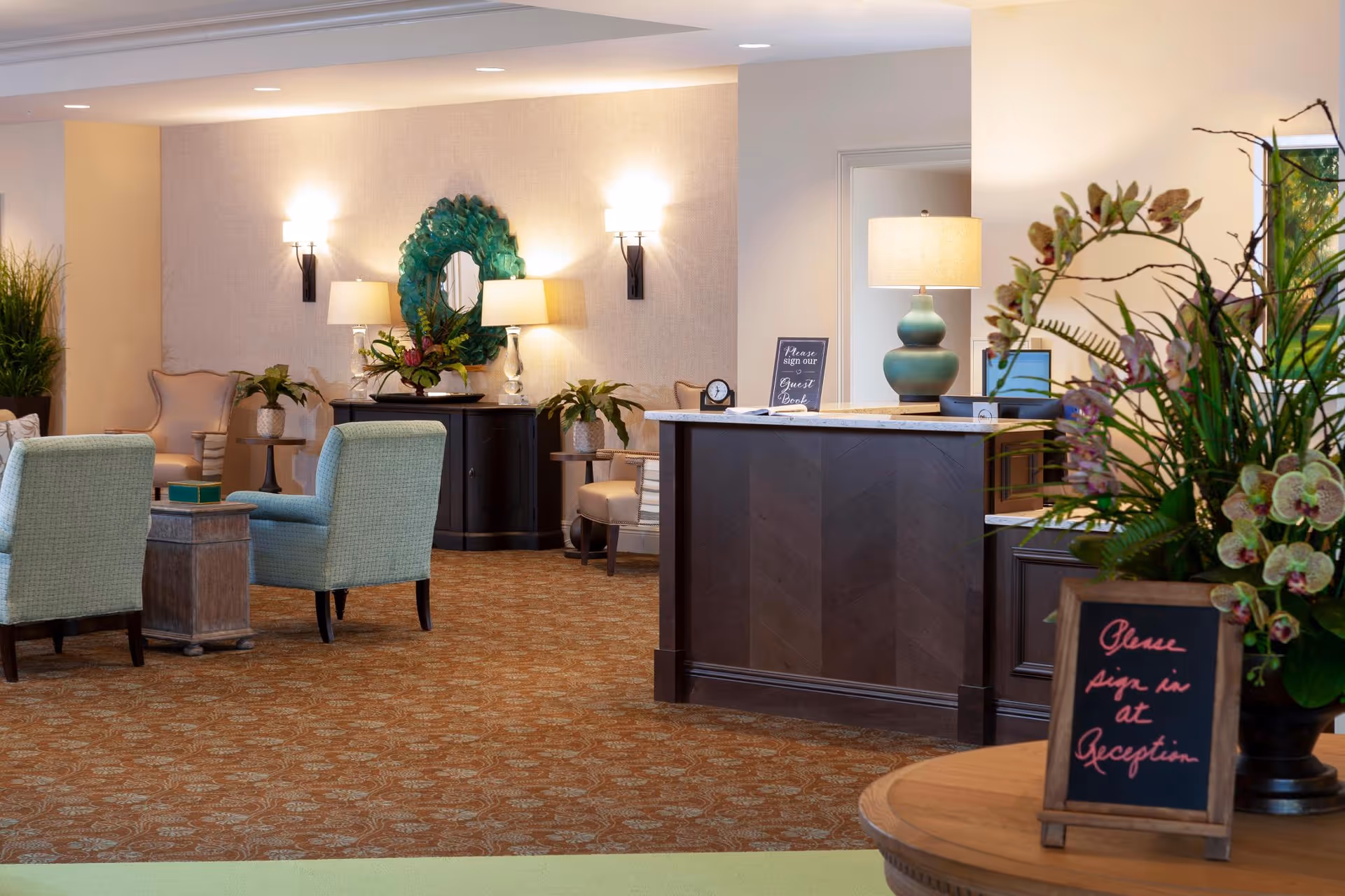 Reception lobby with a front desk, seating area, lamps, and decorative plants.