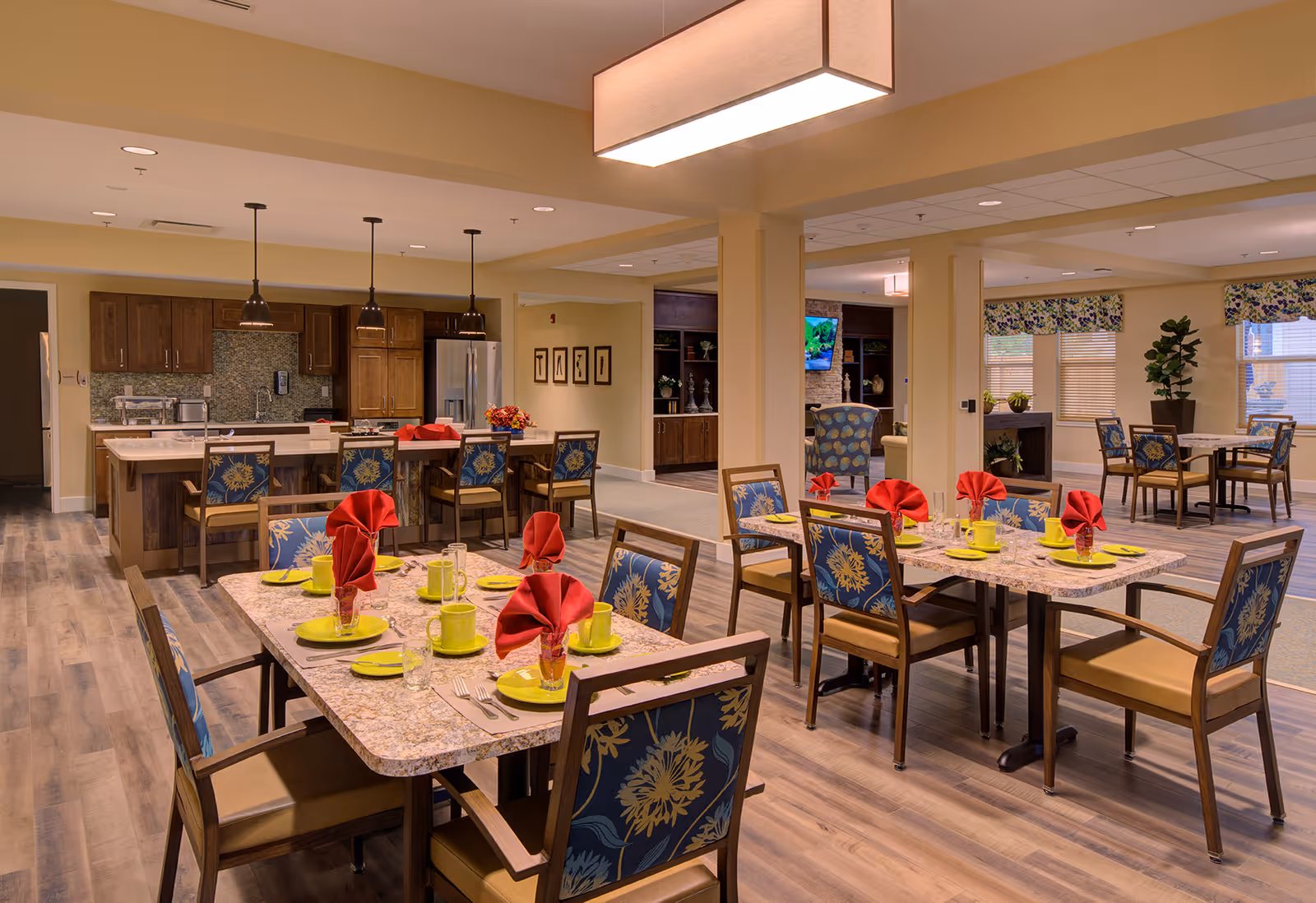 Bright, open dining room with multiple set tables and chairs and an open kitchen in the background.