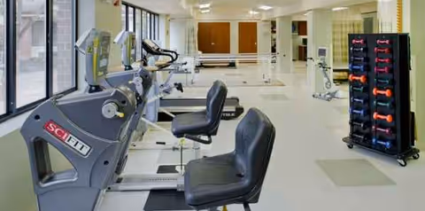 Bright interior senior gym with treadmills, bikes, weights, and a dumbbell rack.