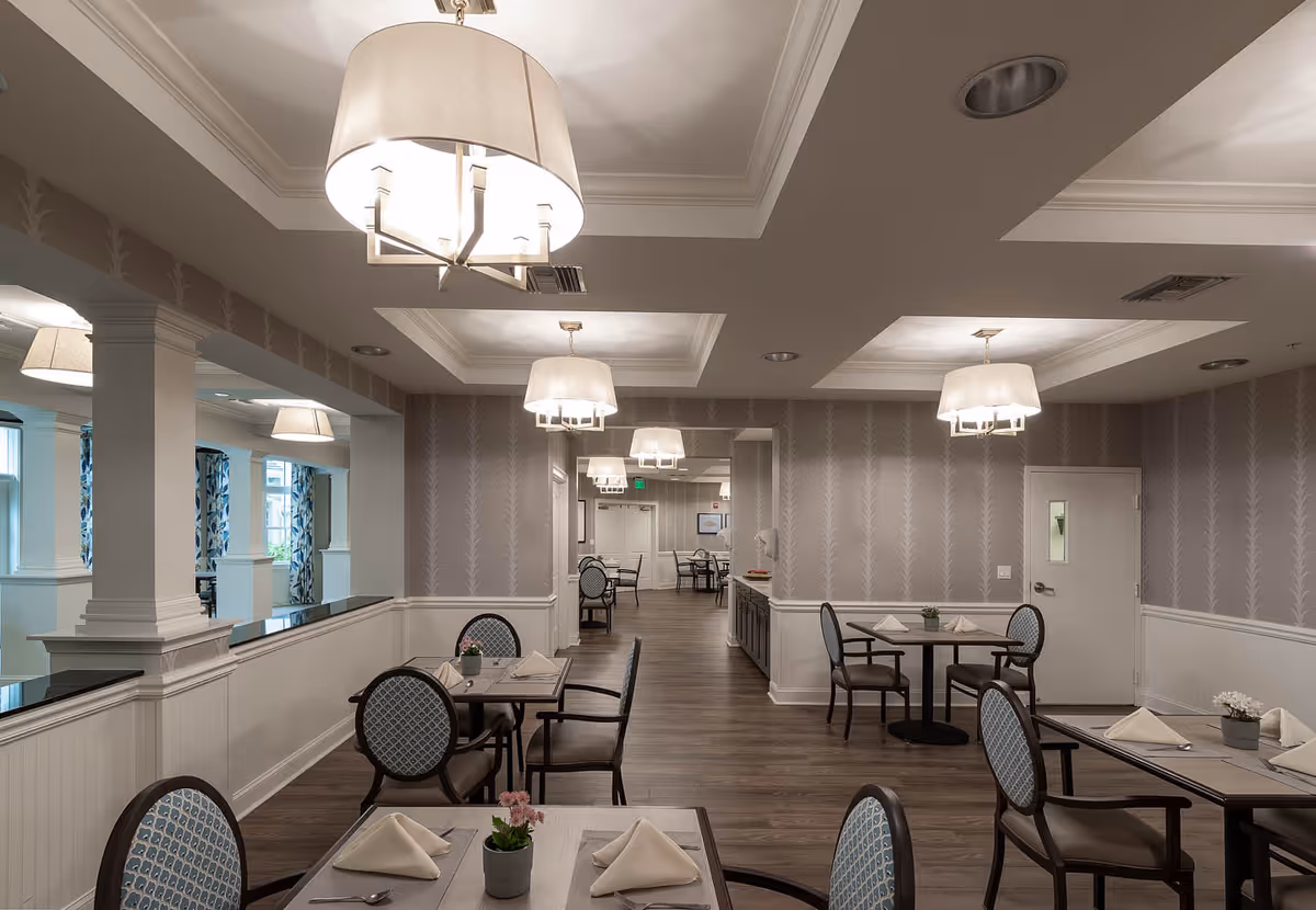 Dining room with multiple set tables and chairs, pendant lights, and soft gray patterned wallpaper.