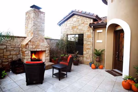 Stone-walled outdoor patio with fireplace, wicker chairs, and pumpkins near the entrance.