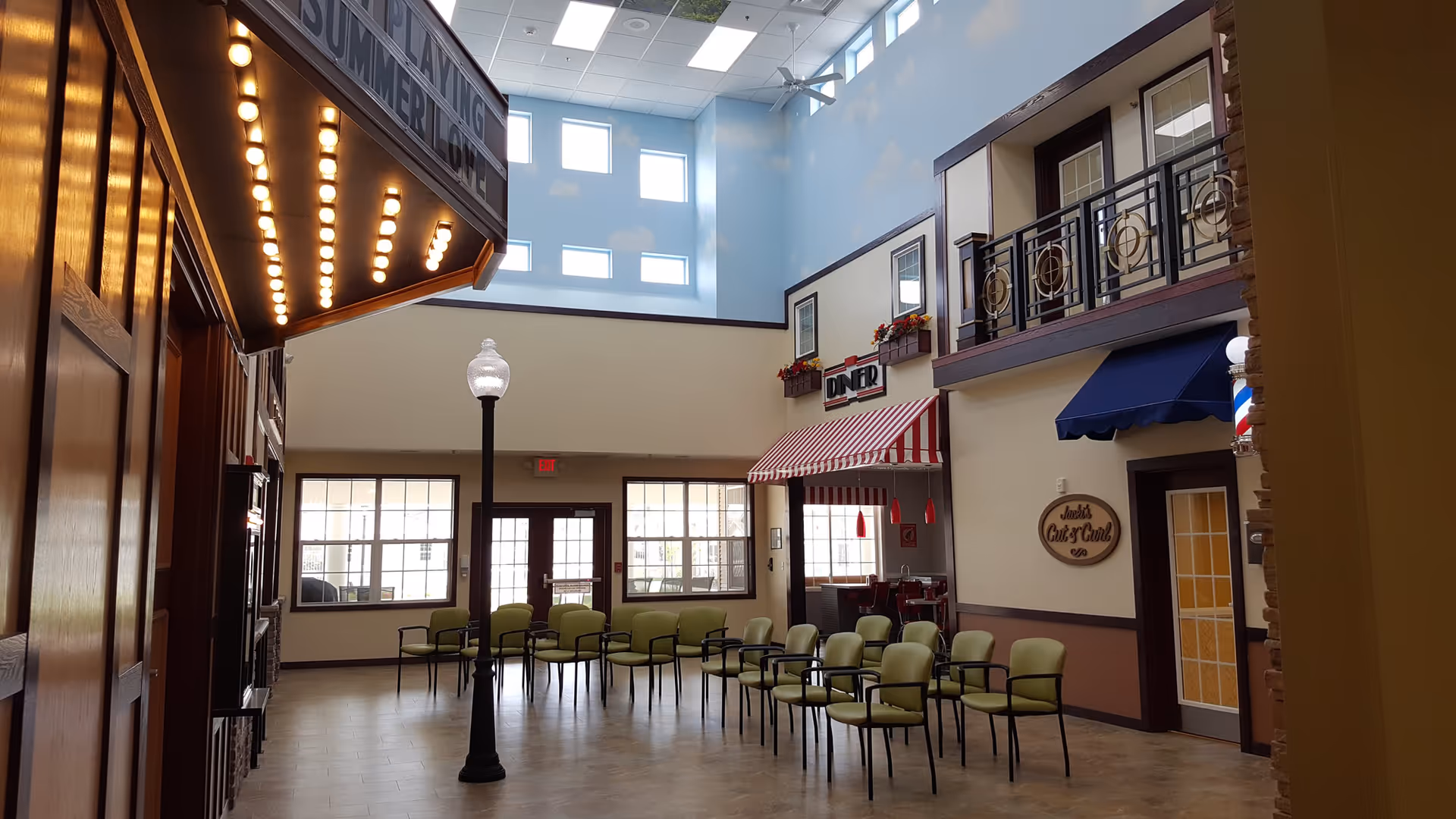 Bright two-story indoor common area with rows of chairs, a lamppost, and faux storefronts including a diner under a high skylight ceiling.