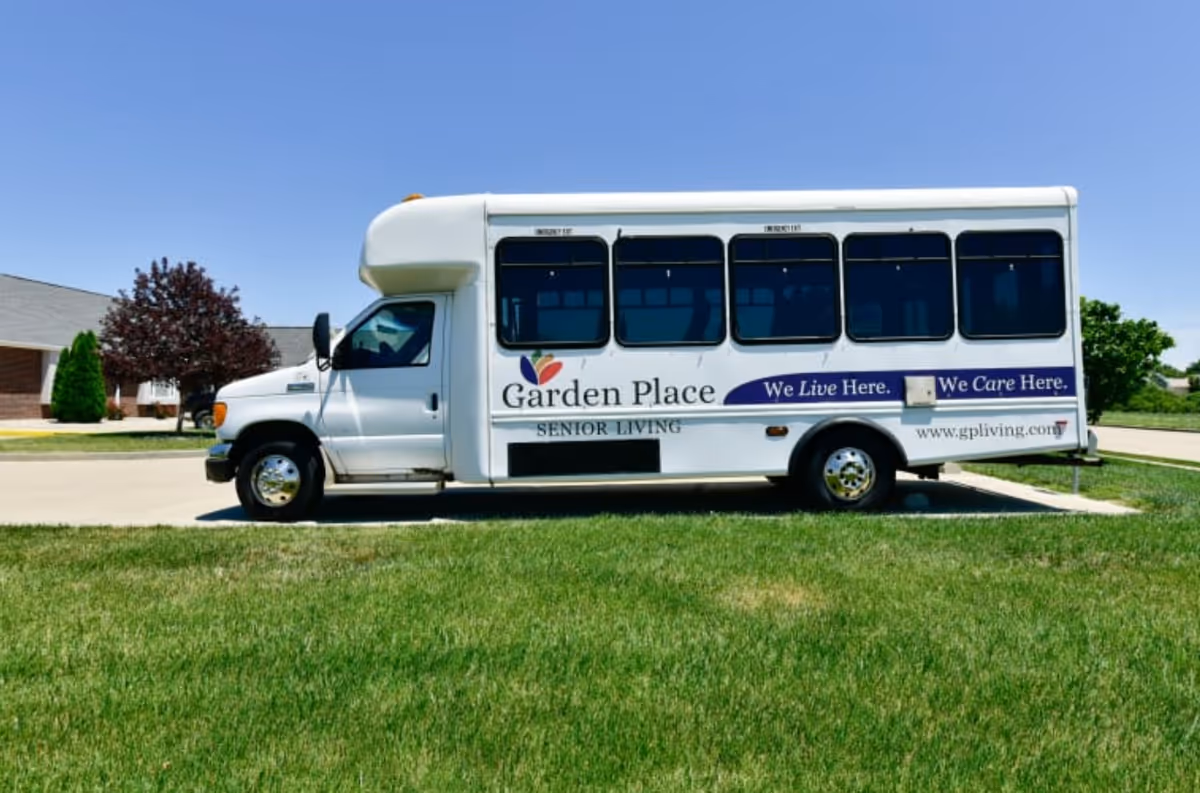 White Garden Place Senior Living bus parked on a grassy lot with a building in background.