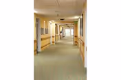 Long carpeted interior hallway in a senior living facility with handrails, doors on both sides, and framed pictures on the walls.