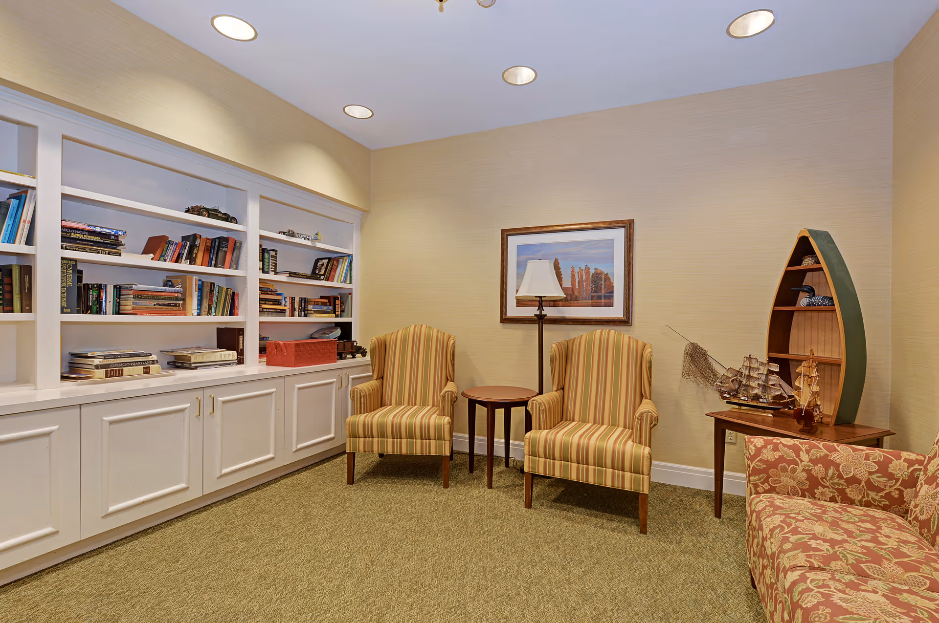 Cozy interior seating area with built-in bookshelves, two striped armchairs, side tables and nautical decor.