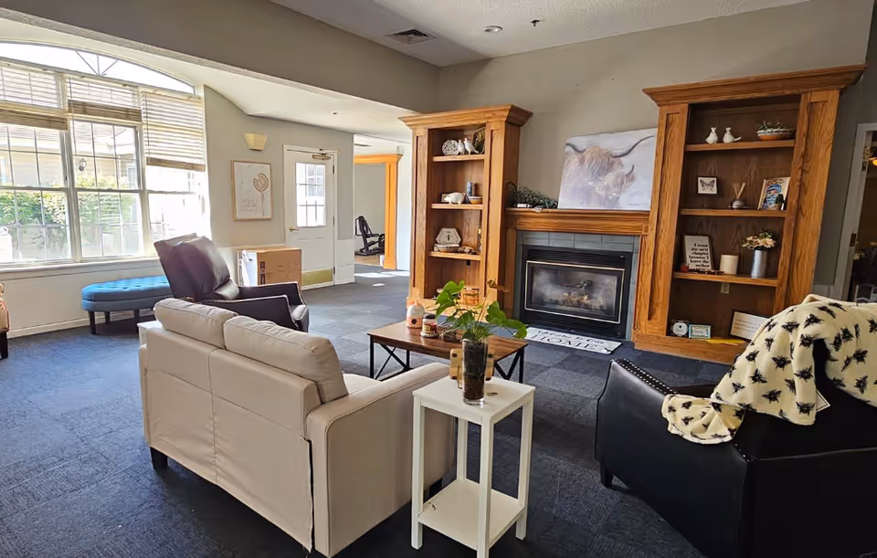 Cozy living room with beige sofa, wooden shelves, fireplace, and large window.