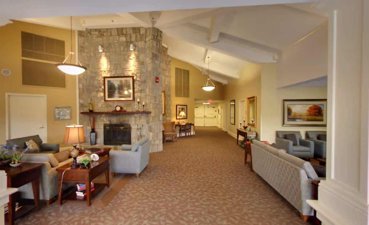 Spacious senior living common room with a stone fireplace, high beamed ceiling, and multiple seating areas.