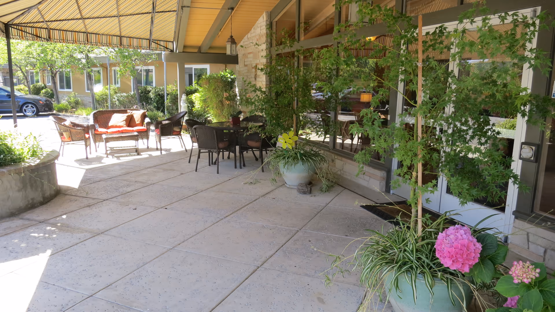Covered front entrance patio with outdoor seating, potted plants, and a tiled walkway leading to glass doors.