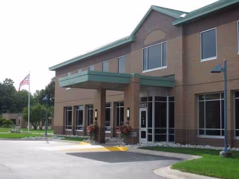 Exterior view of a senior care facility entrance with green canopy and parking.