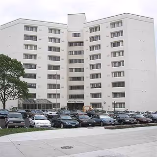 White multi-story senior living building with a large parking lot in front.