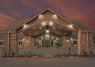 Front entrance of a brick health and rehabilitation building with a covered, well-lit porte-cochère under a purple evening sky.