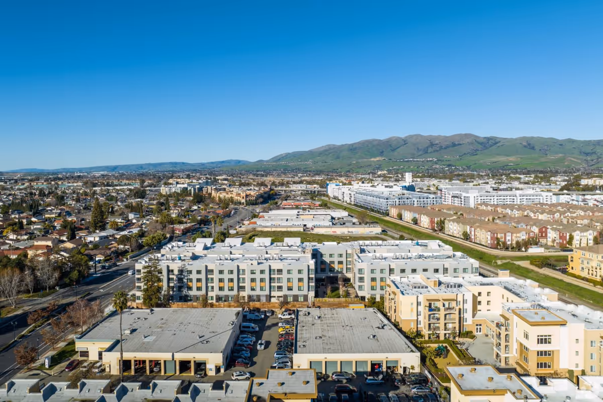 Aerial view of Ivy Park at Milpitas with apartment buildings, parking lots and surrounding neighborhood against distant hills.