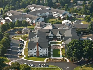 Aerial view of Brandon Oaks Life Plan Community showing multiple connected residential buildings surrounded by trees, parking lots, and landscaped green areas.
