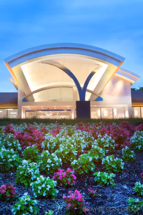 Front entrance of a senior living facility with colorful flower beds and modern arches.