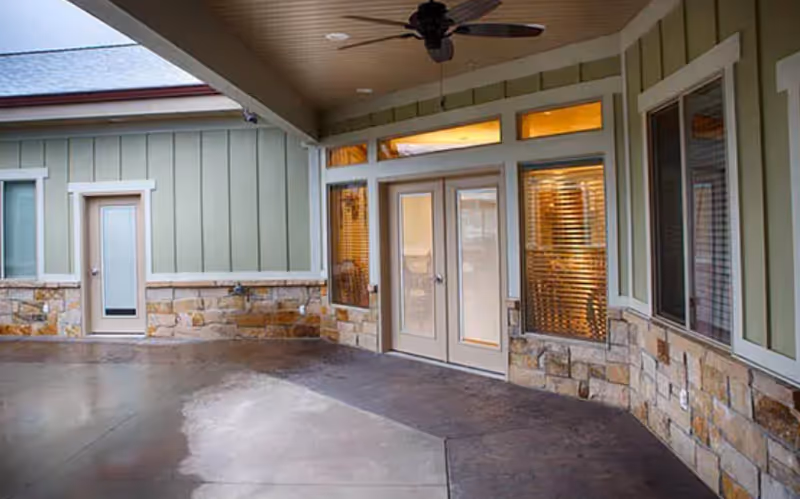 Covered exterior entryway with stone-clad lower walls, green siding, double glass doors and a ceiling fan.