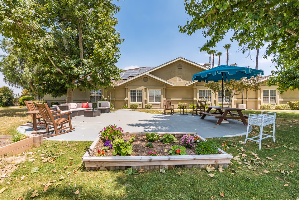 Outdoor patio area with seating, a picnic table and raised flower bed in front of a single-story beige building.