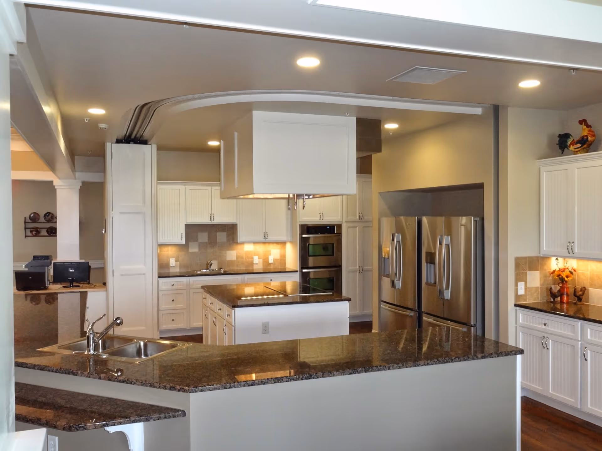 Spacious modern kitchen with granite countertops, white cabinetry, a central island, double stainless steel refrigerators and built-in ovens.
