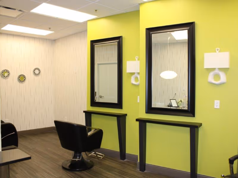 Interior salon styling area with two mirrors on a lime-green wall and black salon chairs.