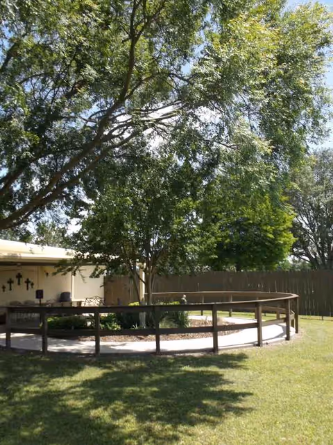 Outdoor courtyard with circular path, wooden railing, trees, and lawn near a building.