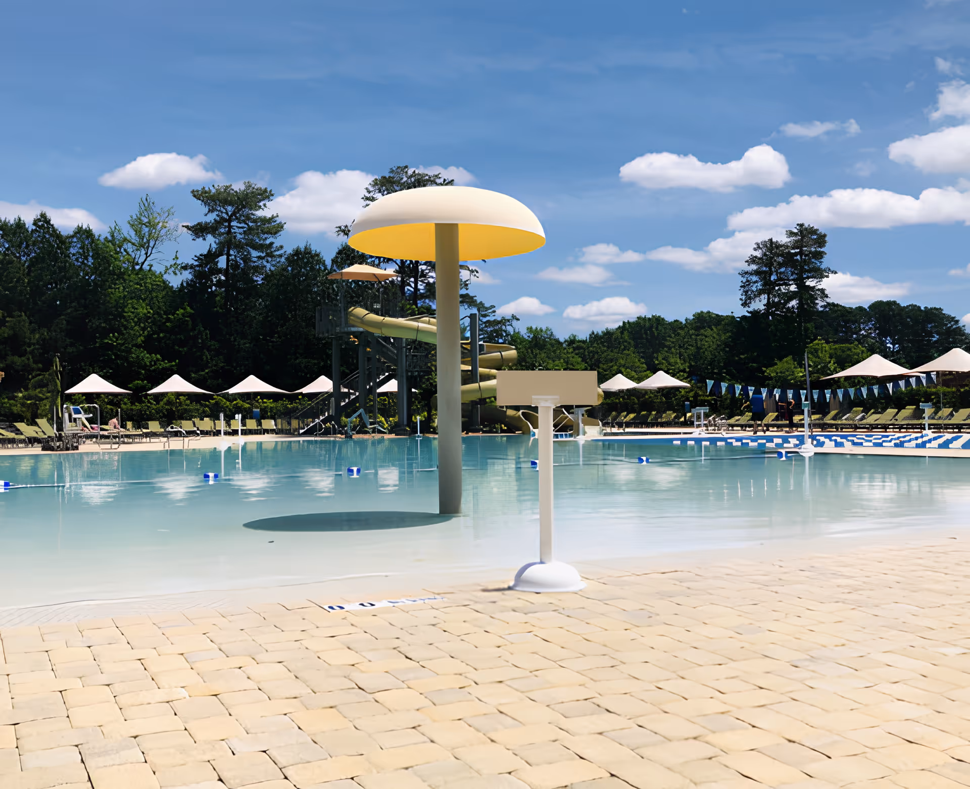 Outdoor swimming pool area with a large mushroom-shaped water feature, a water slide in the background, lounge chairs with umbrellas, and a clear blue sky with scattered clouds.