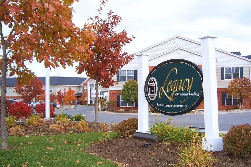 Entrance sign reading 'Legacy at Cranberry Landing' in front of a senior living building with autumn trees and landscaping.