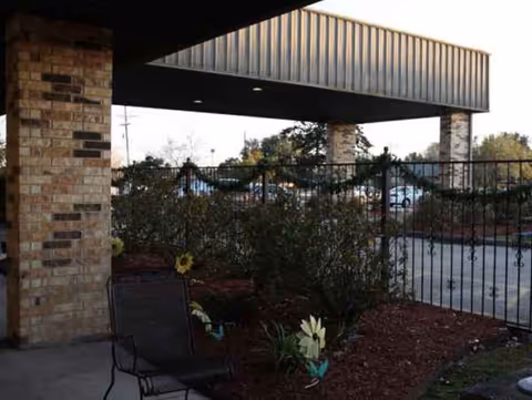 Outdoor covered walkway with brick columns, railing, and landscaped garden beds.