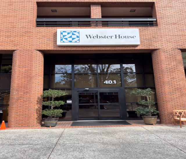 Main entrance of Webster House building with glass double doors, the number 401, a sign above, and potted plants at the doorway.