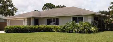 Front exterior of a single-story beige assisted living home with a manicured lawn.