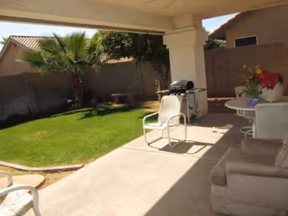 Covered patio with lawn, chairs, a grill, and a table with flowers.