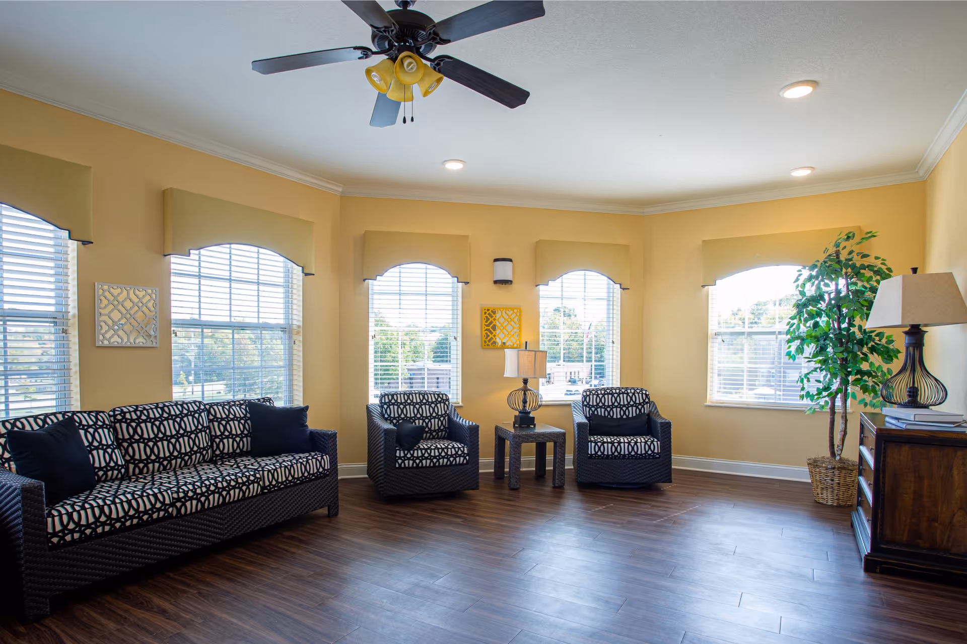 Bright communal sitting area with a patterned sofa and two matching armchairs arranged around a small table beneath arched windows.