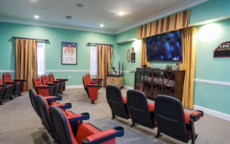 A small theater-style entertainment room with rows of red and black reclining chairs facing a wall-mounted TV in a mint-green room.