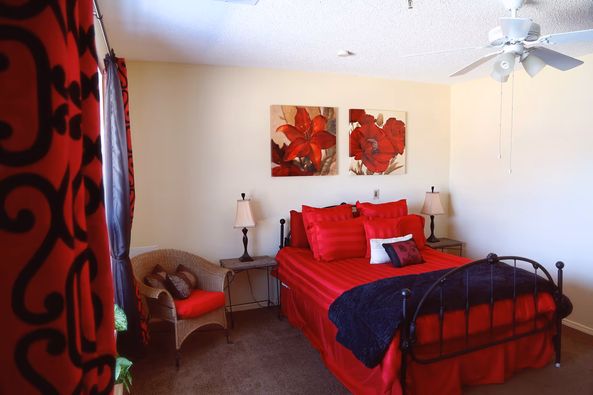 Red-accent bedroom featuring a metal bed, lamps, and wicker chair.
