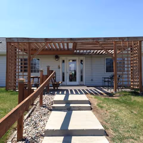 Front entrance of a single-story assisted living facility with a wooden pergola and walkway.