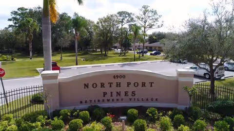 Entrance sign for North Port Pines Retirement Village with landscaping and palm trees