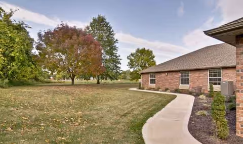 Exterior of a brick senior living facility with curved walkway, lawn, and trees.