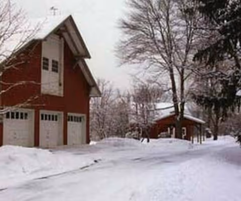 Snow-covered road leads to a red building with three garage doors and bare trees.